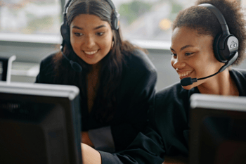 Zwei Mitarbeiterinnen tragen Headsets und sitzen vor Computerbildschirmen.