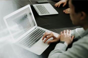 Eine Person sitzt an einem Tisch und arbeitet an einem Laptop.
