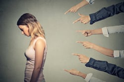 Concept of accusation guilty person girl. Side profile sad upset woman looking down many fingers pointing at her back isolated on grey office wall background. Human face expression emotion feeling