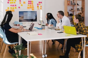 Marketingteam sitzt um einen Tisch und arbeitet an Laptops im Austausch miteinander.  