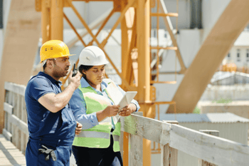 Ein Bauarbeiter und eine Bauplanerin stehen auf einer Baustelle.