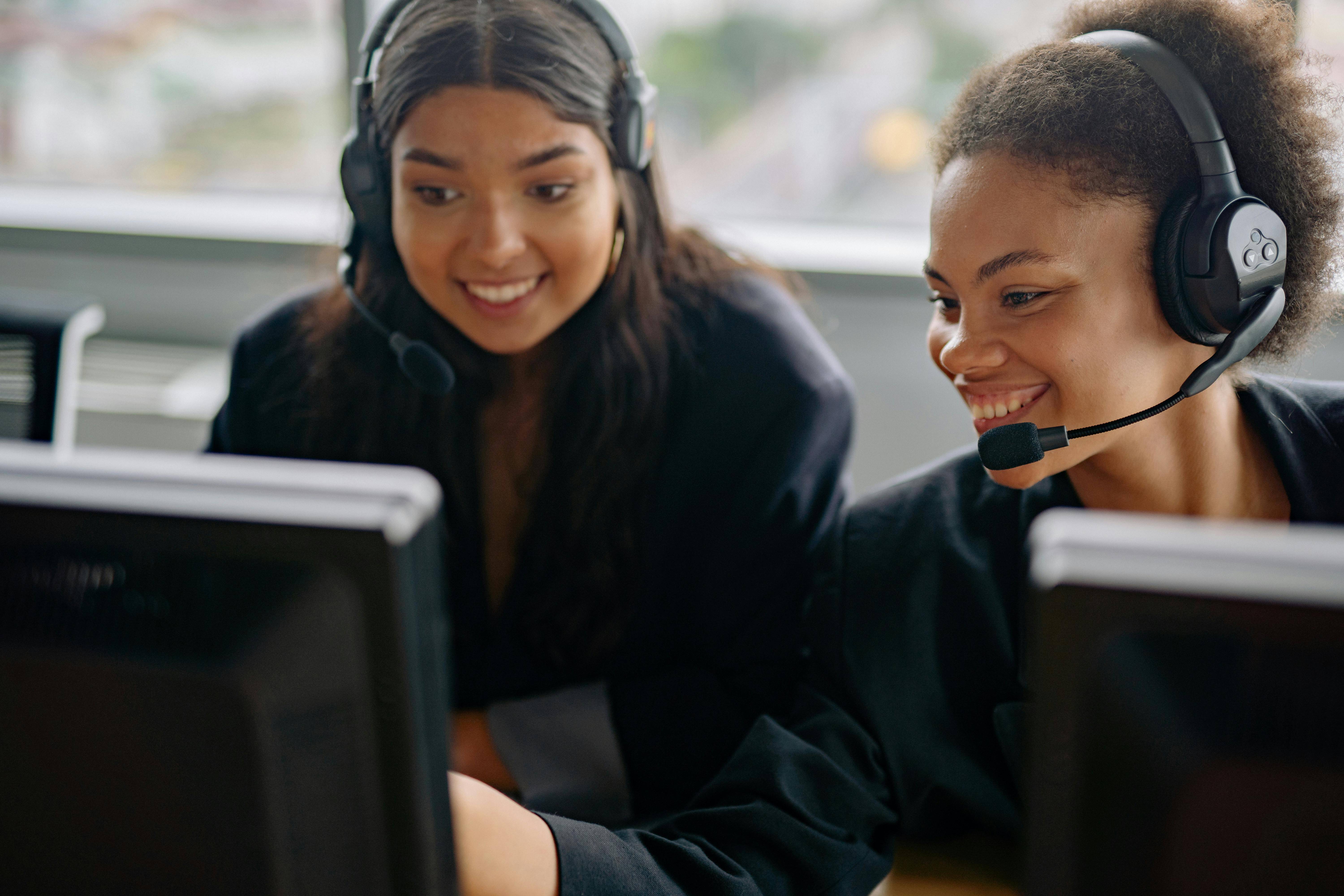 Zwei Mitarbeiterinnen tragen Headsets und sitzen vor Computerbildschirmen.