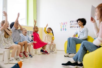 Eine Gruppe von Kindern im Klassenzimmer hebt die Hände, um am Unterricht teilzunehmen. 