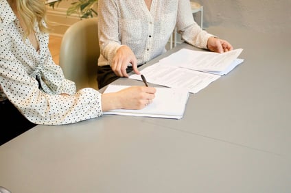 Zwei Frauen sitzen an einem Tisch im Büro und prüfen Dokumente.