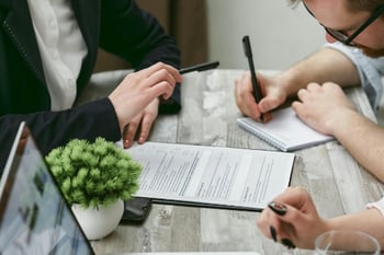 Drei Personen sitzen an einem Tisch und machen Notizen.&nbsp;