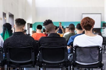 Eine Gruppe von Schüler:innen hören bei einer Präsentation zu. 