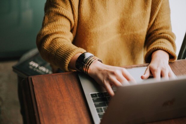 Eine Frau sitzt an einem Tisch und arbeitet an ihrem Laptop.